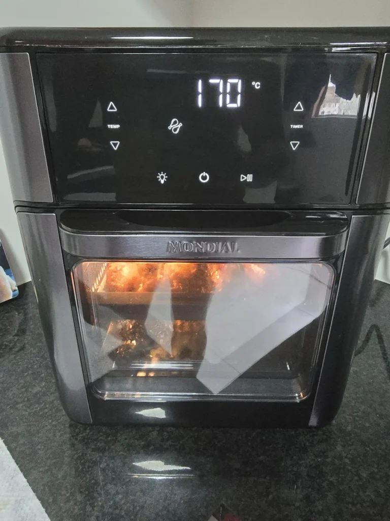 Air Fryer Forno Mondial 12L em funcionamento com carne assando no rack interno e display digital ligado.