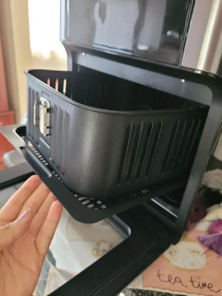 Usuário retirando o cesto antiaderente da Air Fryer Forno Mondial 12L, demonstrando a facilidade de manuseio.
