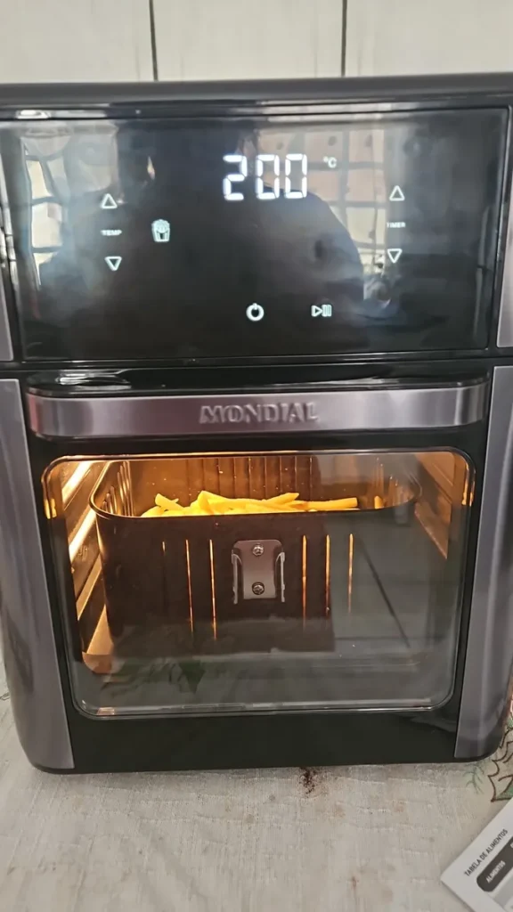 Batatas fritas sendo preparadas no cesto da Air Fryer Forno Mondial 12L, visíveis através do visor de vidro.